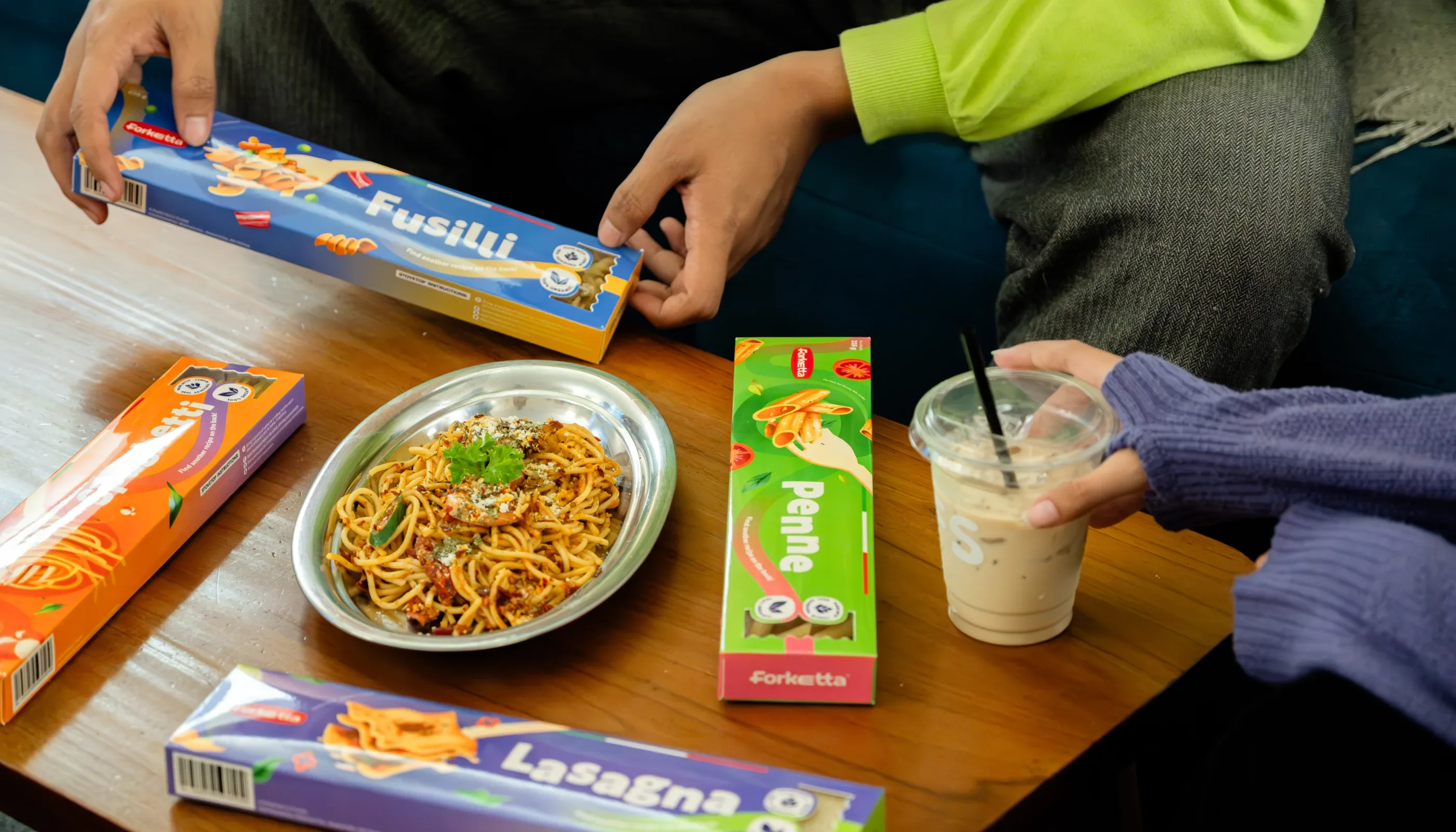 Forketta pasta boxes and a plated dish styled on a wooden table with iced drinks